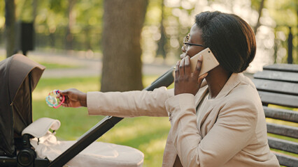 Multitasking mother holding baby rattle and talking on phone, taking care of infant