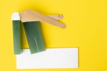 View of wax with wooden sticks and Depilatory Paper in yellow background with copyspace