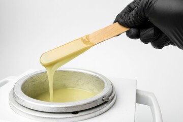 Human hand holding wooden sticks with wax over wax melter