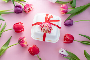 Colorful red double tulips lie around a white dessert gift box with a red ribbon. View from above