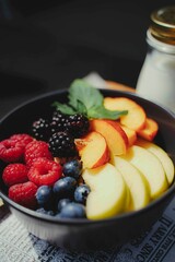 Closeup of different fresh fruits and various berries in a black bowl with a glass of milk