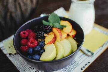 Closeup of different fresh fruits and various berries in a black bowl with a glass of milk