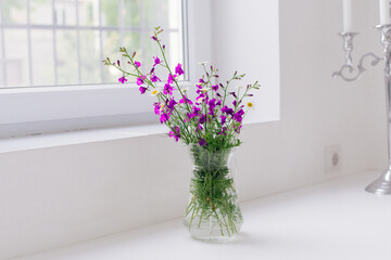 A vase with beautiful wildflowers on a white table near the window