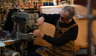 adult craftsman sitting adding thread in a sewing machine to start sewing parts of a chair made of...
