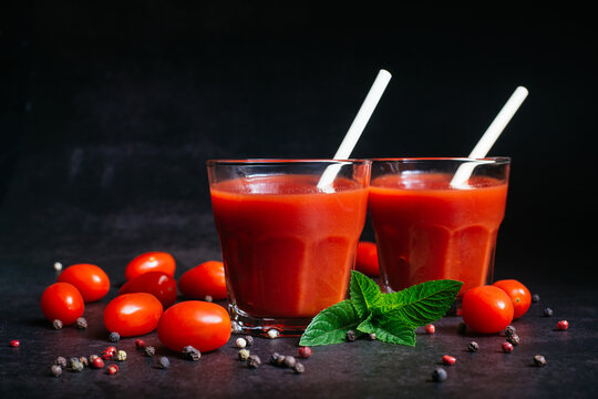 Fresh tomato juice in a glass with tomatoes, pepper on a dark background