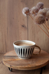 Modern cup of coffee on stylish wooden pad, wooden wall, natural interior, driers flowers, cozy and minimalistic style
