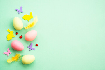 Fototapeta na wymiar Easter background. Eggs, rabbit, spring flowers and butterfly. Flat lay mock up at green background.