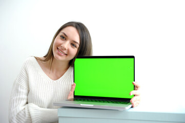 beautiful young girl in a white sweater shows a laptop with a chromakey She smiles advertises a product good presentation joy success win sale nice positive emotions on a white background Woman