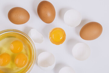 Whole brown eggs and cracked white eggs half with a yolk inside near the glass bowl with egg yolks and egg whites on bright background. Close up, selective focus. Top view.
