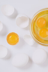 Whole white eggs and cracked white eggs half with a yolk inside near the glass bowl with egg yolks and egg whites on bright background. Close up, selective focus. Top view.