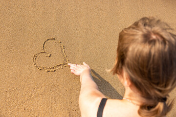 Woman drawing heart shape on the sand with finger