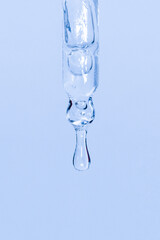 Cosmetic pipette with dripping liquid and drops on a blue background, serum, serum, gel, vitamin,...