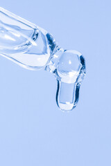Cosmetic pipette with dripping liquid and drops on a blue background, serum, serum, gel, vitamin,...