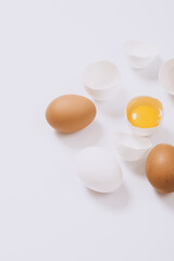 Whole white and brown eggs and cracked egg half with a yolk on bright background. Selective focus.