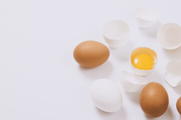 Whole white and brown eggs and cracked egg half with a yolk on bright background. Selective focus.