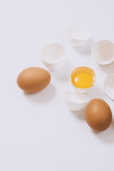 Whole brown eggs and cracked white eggs half with a yolk on bright background. Selective focus.