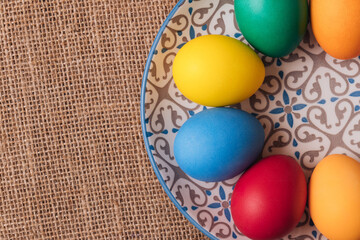 Painted eggs. Colorful Easter eggs in the plate on sackcloth. Macro shot, selective focus. Top view.