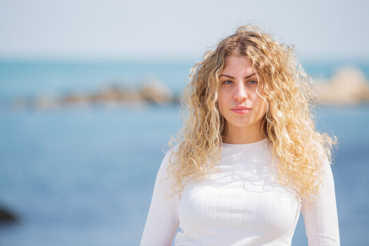 Beautiful Italian girl with long curly hair and white t-shirt at the seashore in the city with palm trees with blur
