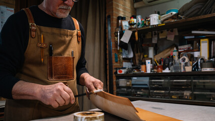 selective focus on the hands of a leather craftsman who dabs the edges of a piece of leather with a waterproof varnish