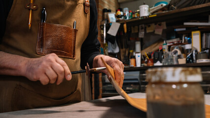 selective focus on the hands of a leather craftsman who dabs the edges of a piece of leather with a waterproof varnish