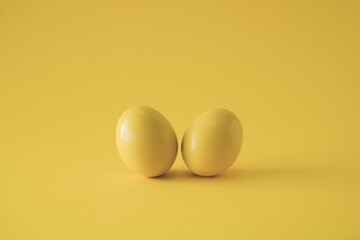 Two yellow colored eggs on yellow background. Minimal Easter concept.
