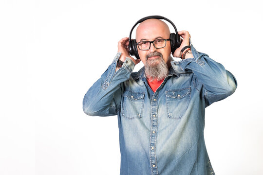 hombre de mediana edad calvo con perilla y gafas escuchando musica con auriculares en el movil entusiasmado con camisa vaquera