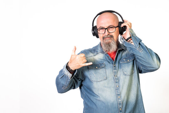 hombre de mediana edad calvo con perilla y gafas escuchando musica con auriculares en el movil entusiasmado con camisa vaquera