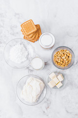 Ingredients for cheesecake. Cookies, caramel, peanuts, butter, cream cheese, powdered sugar, cream in glassware on table. Top view.
