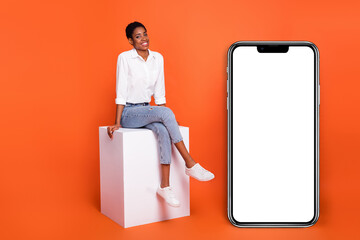 Full size photo of beautiful appearance female sitting podium near phone advertisement isolated on orange color background