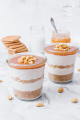 Cheesecake in a jar. Layers of grinded cookies, caramel, peanuts and  cream cheese. Covered in caramel and decorated with peanuts. Selective focus. Macro shot.