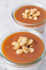 Cheesecake in a jar. Layers of grinded cookies, caramel, peanuts and  cream cheese. Covered in caramel and decorated with peanuts. Close-up photo. Selective focus. Macro shot.