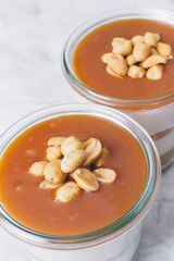 Cheesecake in a jar. Layers of grinded cookies, caramel, peanuts and  cream cheese. Covered in caramel and decorated with peanuts. Close-up photo. Selective focus. Macro shot.