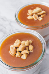 Cheesecake in a jar. Layers of grinded cookies, caramel, peanuts and  cream cheese. Covered in caramel and decorated with peanuts. Close-up photo. Selective focus. Macro shot.