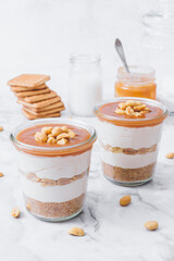 Cheesecake in a jar. Layers of grinded cookies, caramel, peanuts and  cream cheese. Covered in caramel and decorated with peanuts. Selective focus. Macro shot.