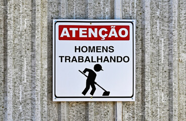 Metal sign indicating MEN AT WORK with words in Portuguese