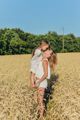 Naklejka na ściany i meble Growing wheat. Food security. A woman holds her little daughter in her arms and stands in a wheat field in summer.