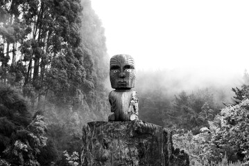 Maori tiki statue surrounded by mist in Waikato Aotearoa New Zealand in nature black and white...