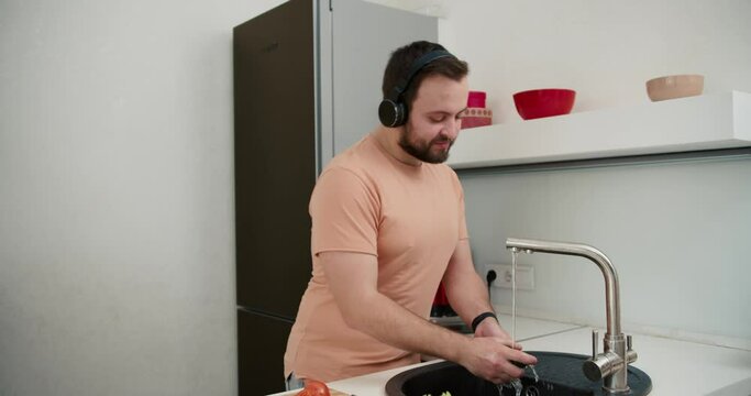 Householder listens to dynamic music in headphones dancing in kitchen at home