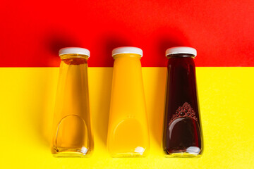 Bottles with yellow and red liquid halthy beverage on yellow and red background. Orange apple cherry
