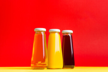 Bottles with yellow and red liquid halthy beverage on yellow and red background. Orange apple cherry