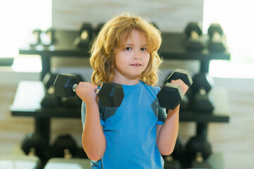 Kid raising a dumbbell. Cute child training with dumbbells. Kids fitness. Kid boy exercising with dumbbells. Healthy kids.
