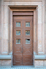 Tall old wooden door with square ornament and broken glass