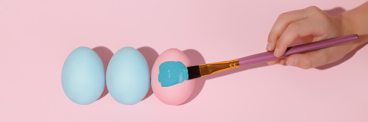Three colored eggs in a row flat lay. Brush paints a pink Easter egg with blue gouache. Easter colored eggs lie in a row flat lay. Banner for website header design with copy space.