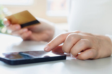 Woman doing online shopping using debit card and mobile. Female hands holding credit card over a mobile sitting at a desk buying goods online from home financial business concept close up online 