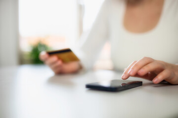 Woman doing online shopping using debit card and mobile. Female hands holding credit card over a mobile sitting at a desk buying goods online from home financial business concept close up online 