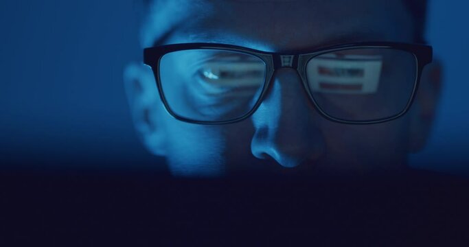 Reflection of scrolling on laptop screen in man's glasses at night