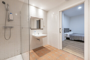 Fototapeta na wymiar A large unfurnished washroom with a floating porcelain sink, glass-enclosed shower, and wall-mounted mirror with access to a bedroom