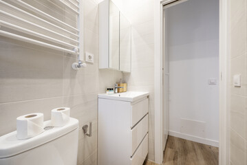 A small bathroom with a white wooden cabinet with drawers, a porcelain sink and a wall cabinet with mirror doors