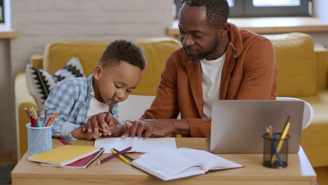 Loving positive african american father teaching little son to write, preparing to school together at home, empty space