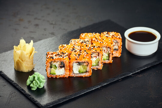 Roll with tobiko caviar, sesame seeds, salmon, eel, cucumber, avocado and cream cheese on dark background. Sushi menu. Japanese food.